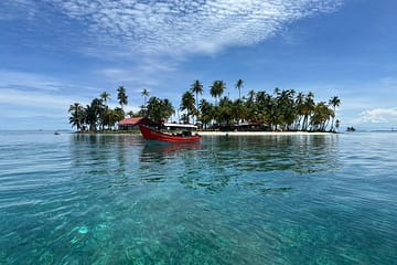 Embarcación llegando a Isla Pelícano, rodeada de aguas cristalinas y palmeras.